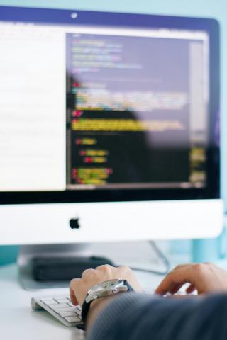 Person typing on a keyboard in front of a large computer.