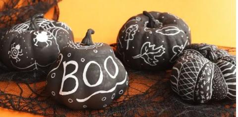 A fake pumpkin painted black with designs drawn on using a chalk marker. 