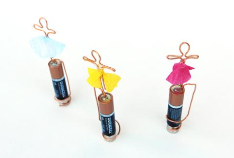 Copper wire shaped into human figures with paper skirts spinning around a battery with the use of magnets.